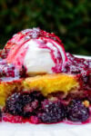 Piece of berry cake topped with vanilla ice cream and berry compote.