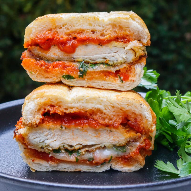 Chicken parmesan sandwich cut in half and stacked on a black plate.