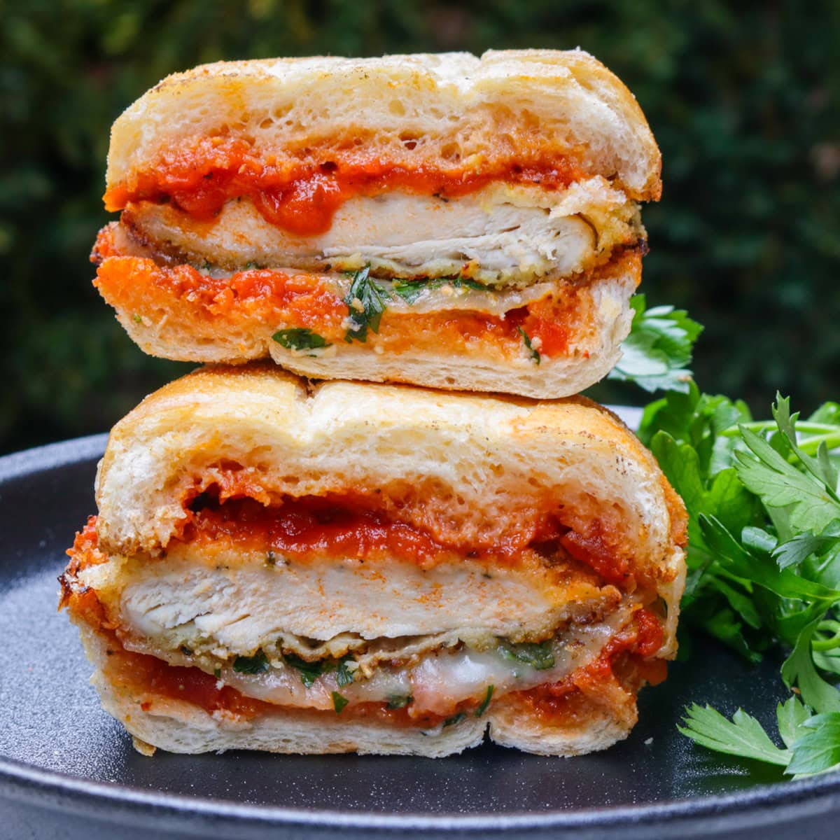 Chicken parmesan sandwich cut in half and stacked on a black plate.