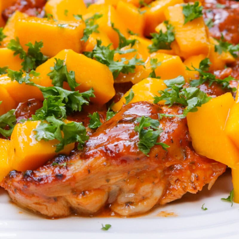Saucy baked chicken thighs topped with diced mango and parsley.