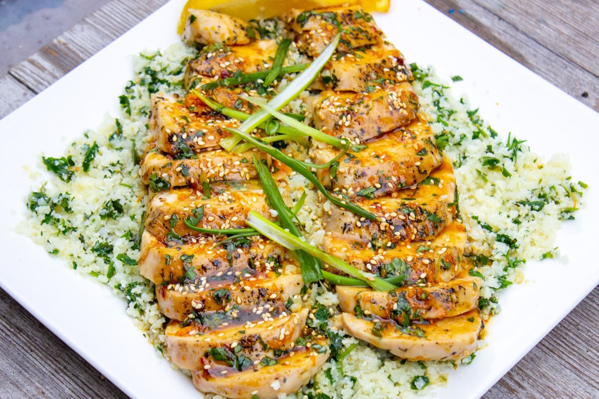 Sliced chicken breast with citrus glaze over cauliflower rice on plate.