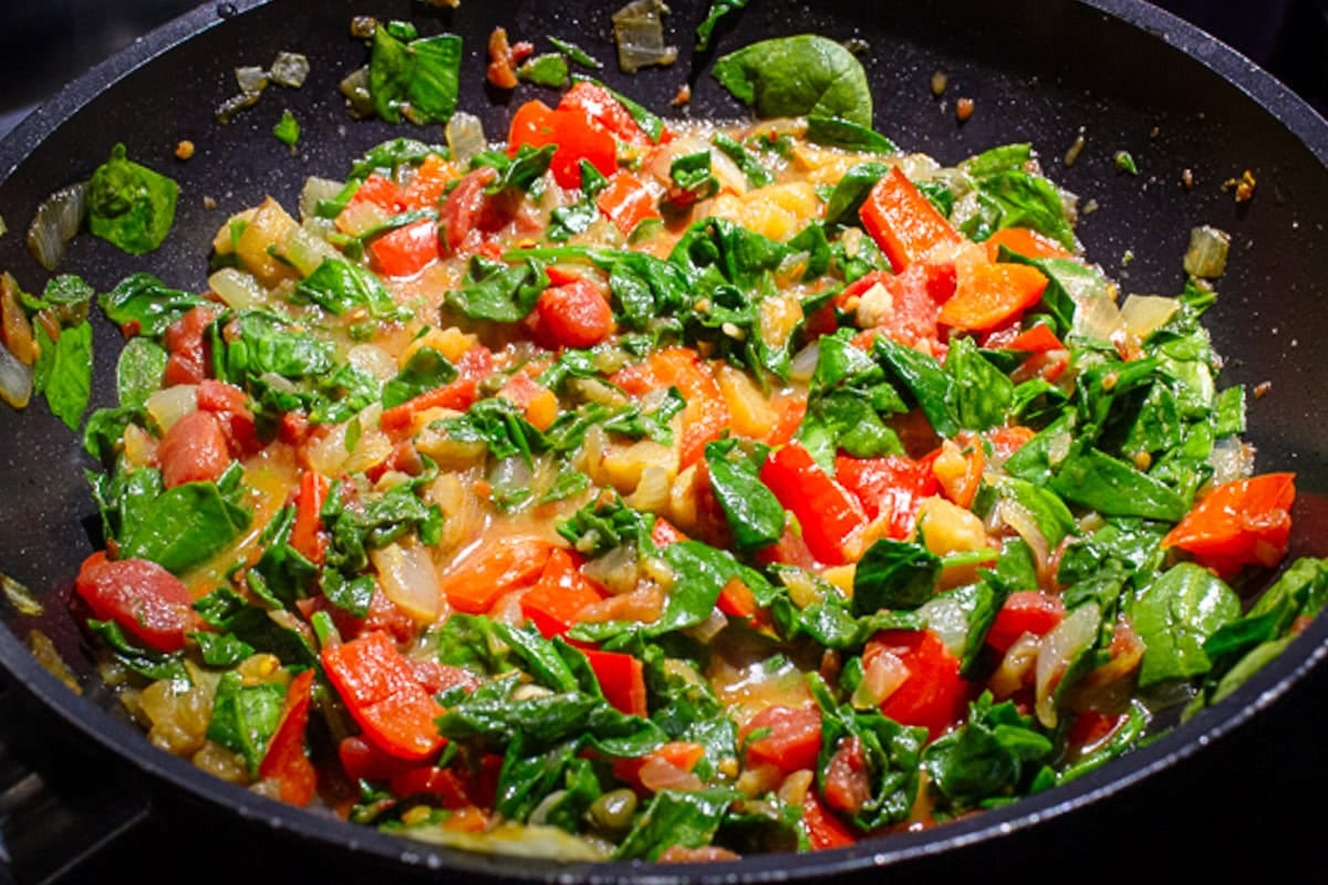 Cooked veggies and spinach in a skillet.