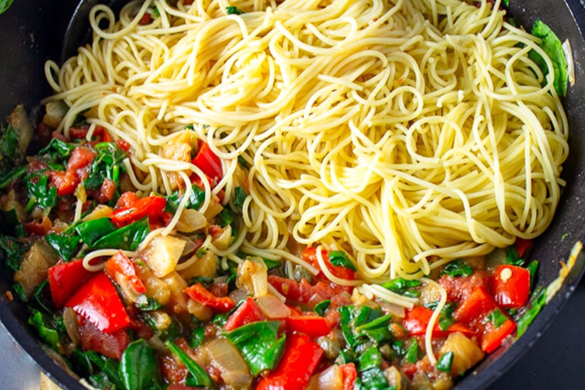 Skillet filled with cooked spaghetti in one half and cooked veggies in the other half.