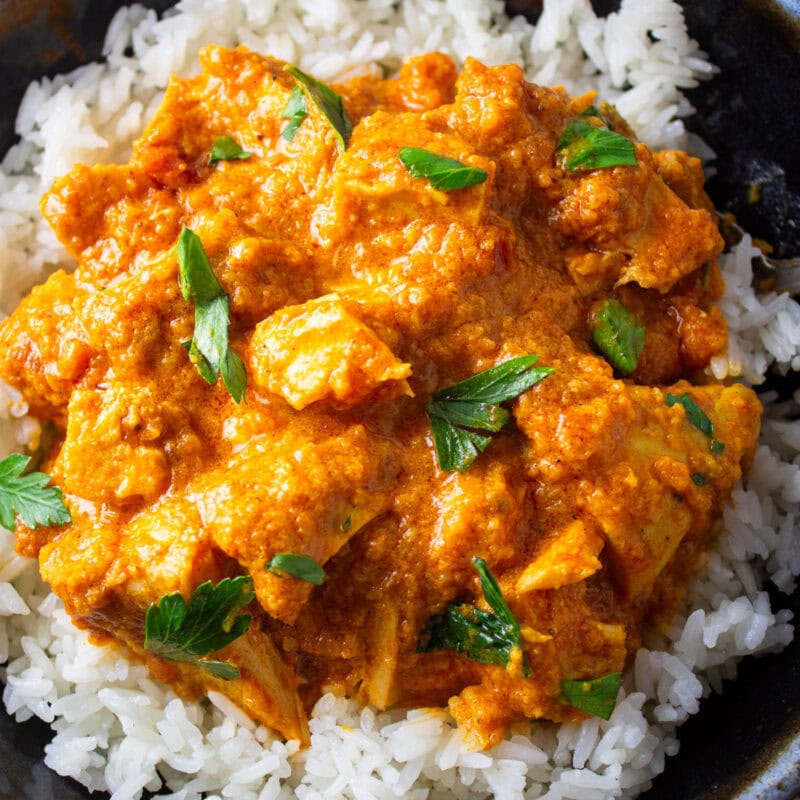 Butter chicken over white rice on plate.