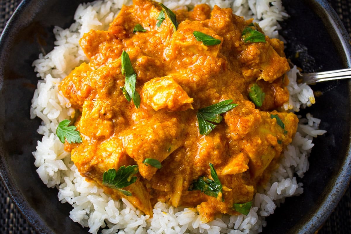 Butter chicken over white rice on plate.