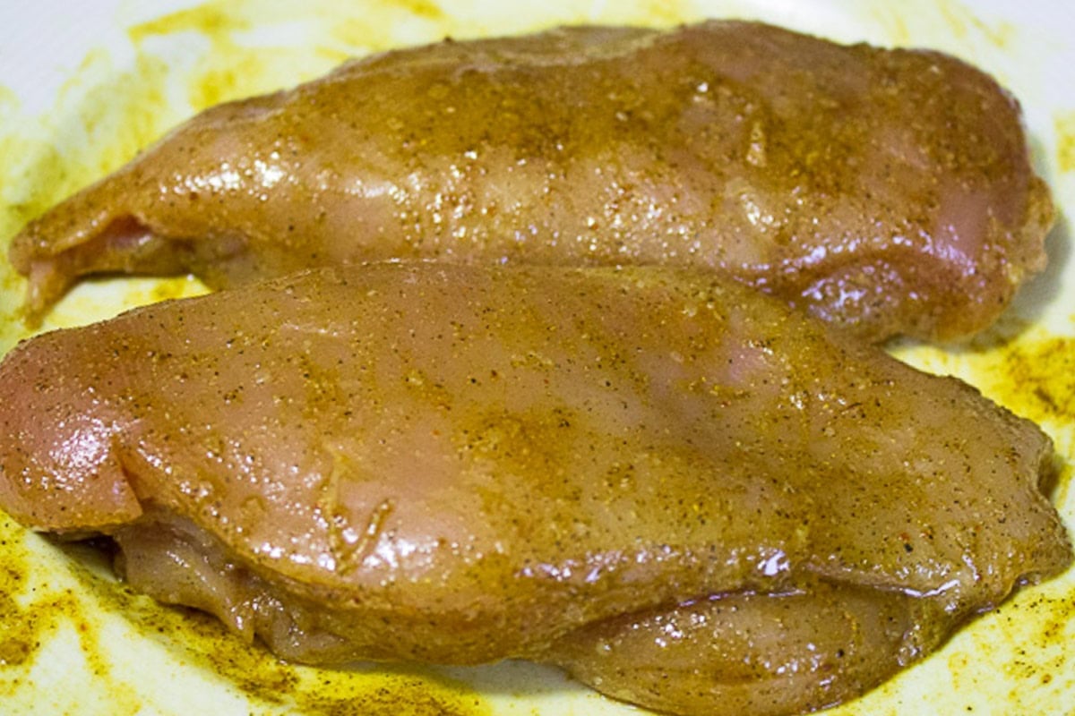 Chicken breasts seasoned with Indian spices on cutting board.
