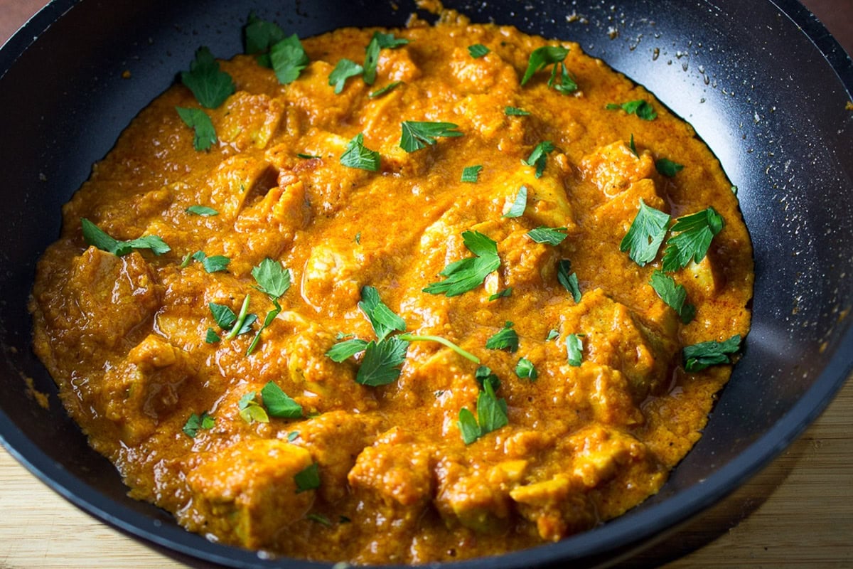 Butter chicken in skillet with parsley on top.