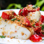 Halibut topped with tomato-caper mixture on plate.
