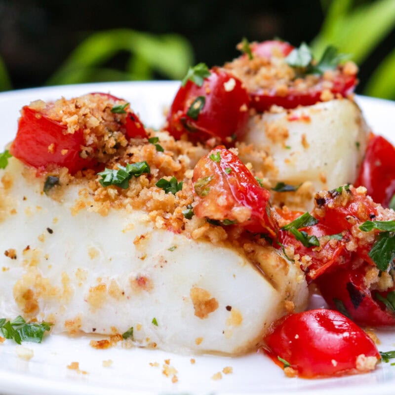 Halibut topped with tomato-caper mixture on plate.
