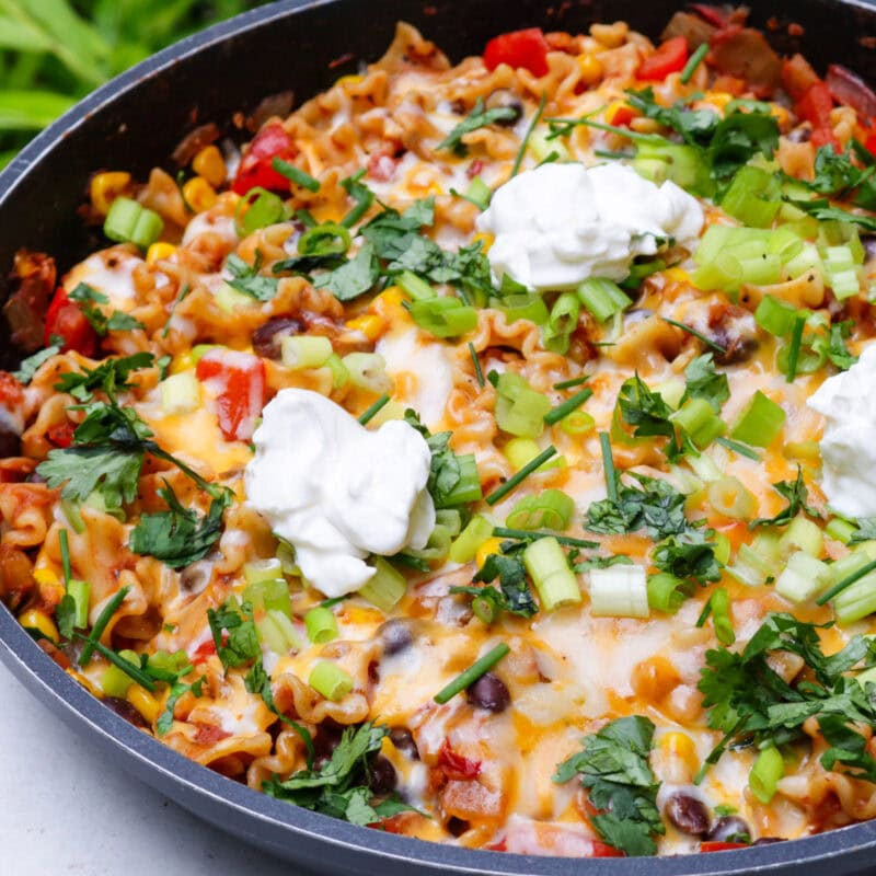 Taco pasta with melted cheese on top and garnished with green onion, cilantro and sour cream in a skillet.