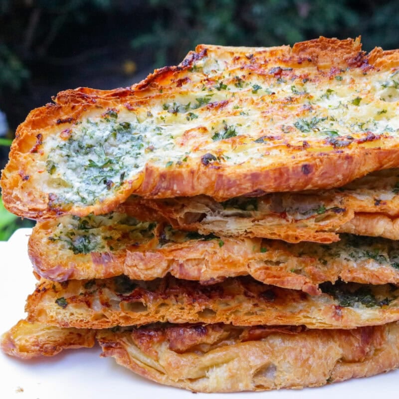Stack of baked garlic bread croissants halves on a plate.