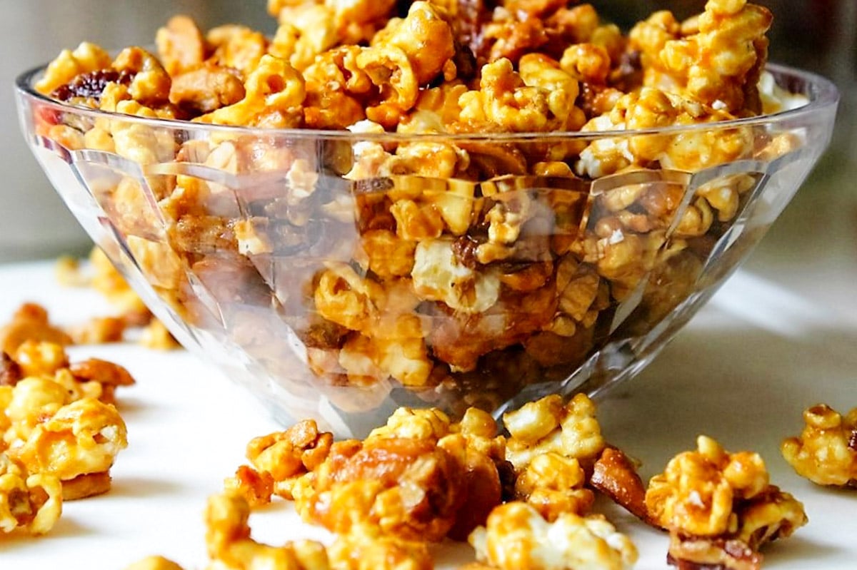 Caramel corn in clear bowl with scattered popcorn around it.