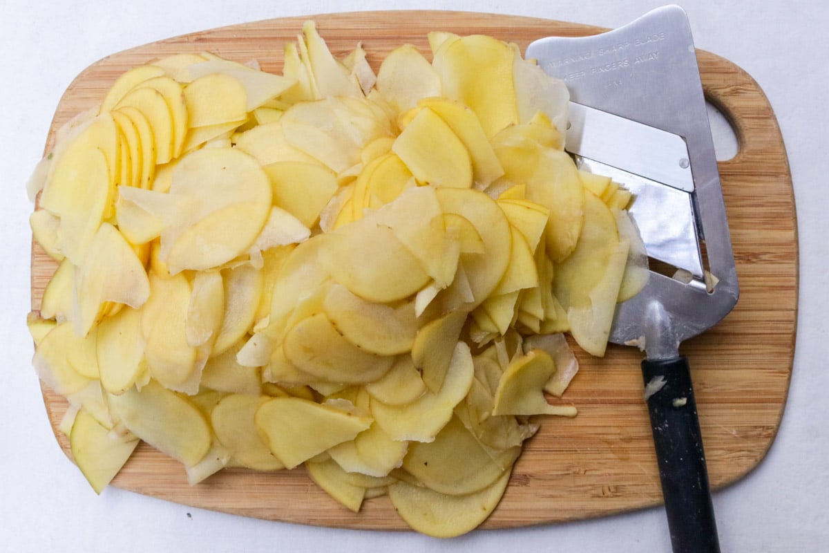 Thinly sliced potatoes on cutting board with mandoline.
