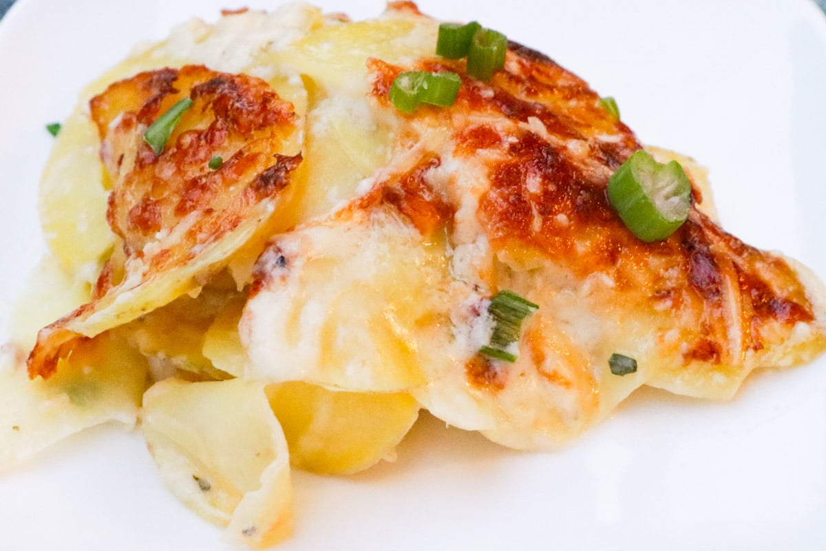 Scoop of cheesy scalloped potatoes with browned crust on a plate.