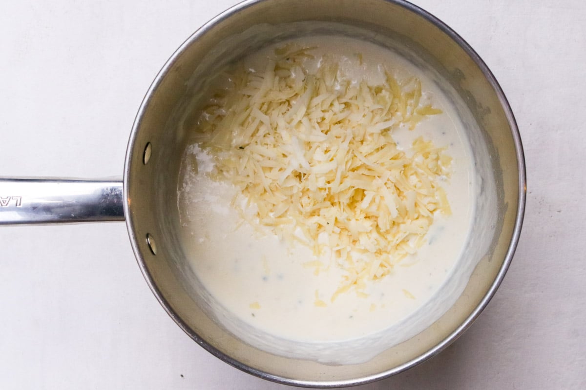 Cream sauce in pot with shredded cheese added.