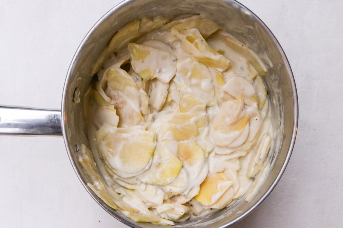 Potatoes combined with cheesy white sauce in pot.