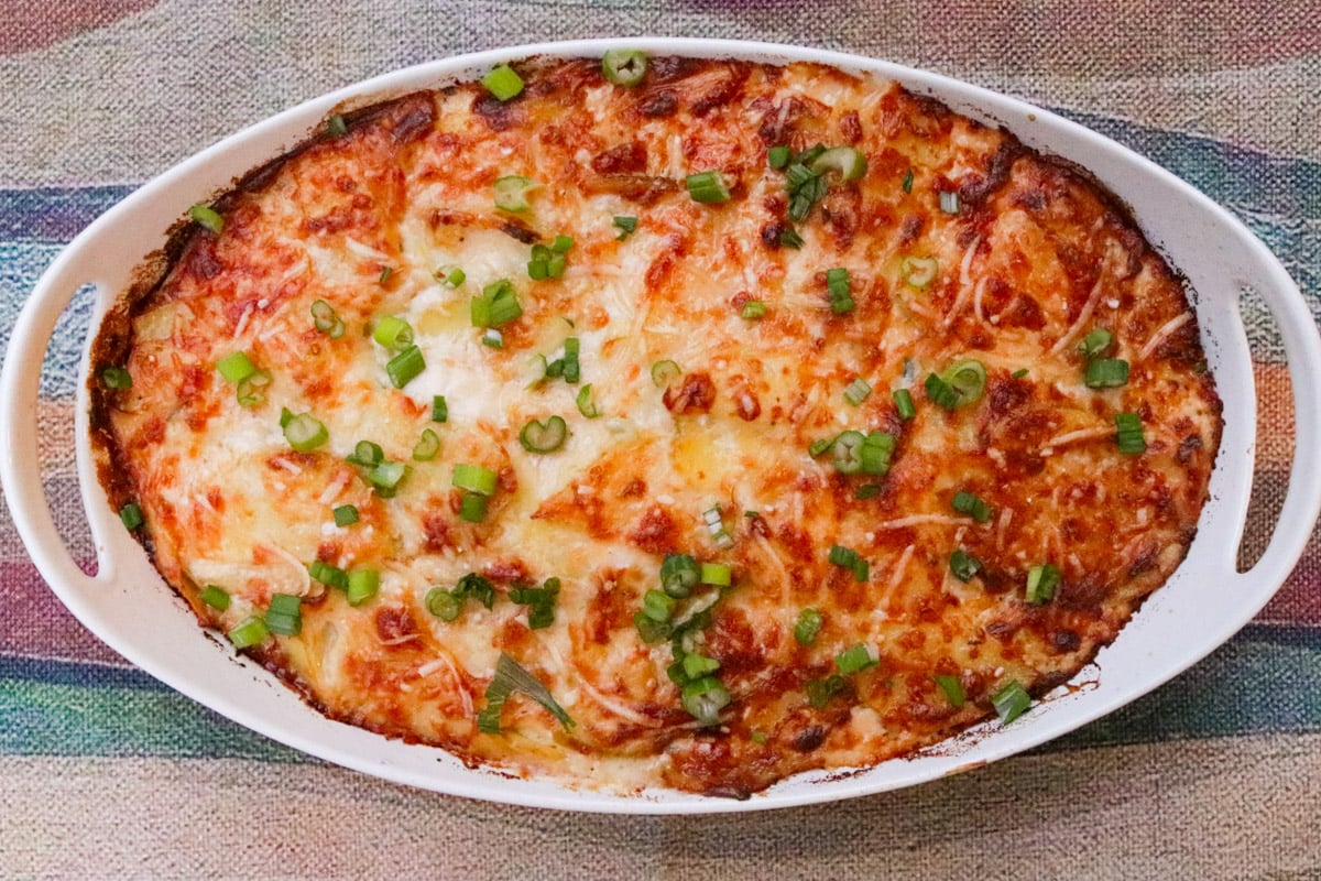 Baked scalloped potatoes in casserole browned on top with garnish of chopped green onions.