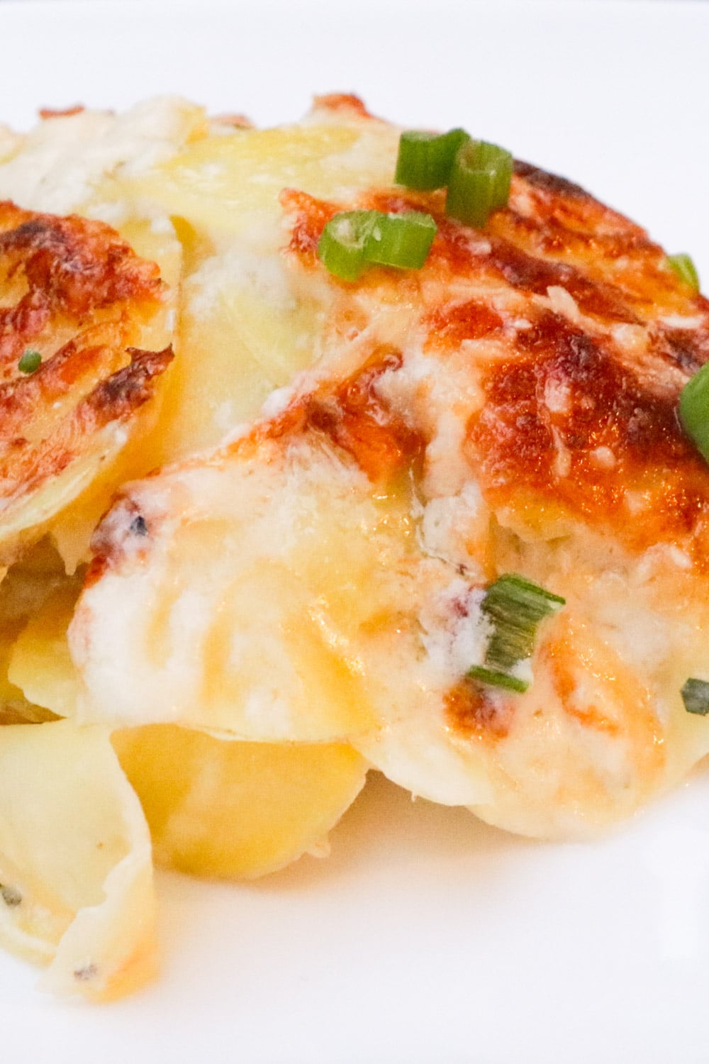 Scoop of cheesy scalloped potatoes with browned crust on a plate.