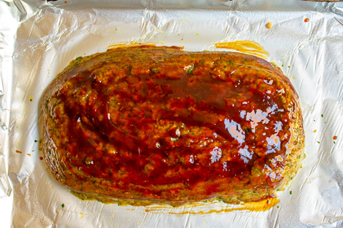 Raw chicken meatloaf with glaze on parchment lined pan.