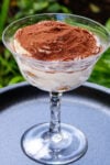 Tiramisu in a glass dessert cup sitting on a plate.