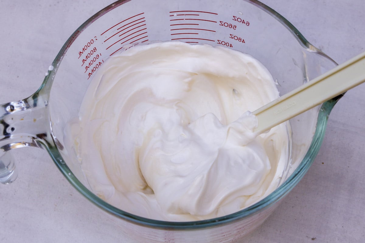 Whipped cream folding in with mascarpone cheese in bowl.