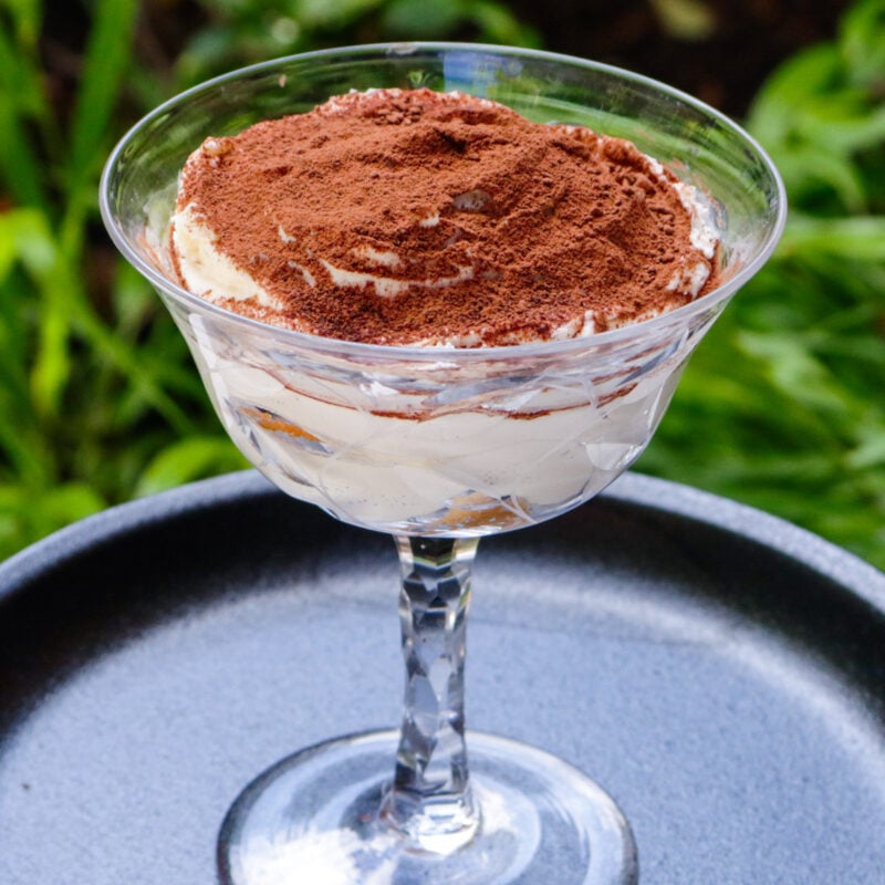 Tiramisu in a glass dessert cup sitting on a plate.