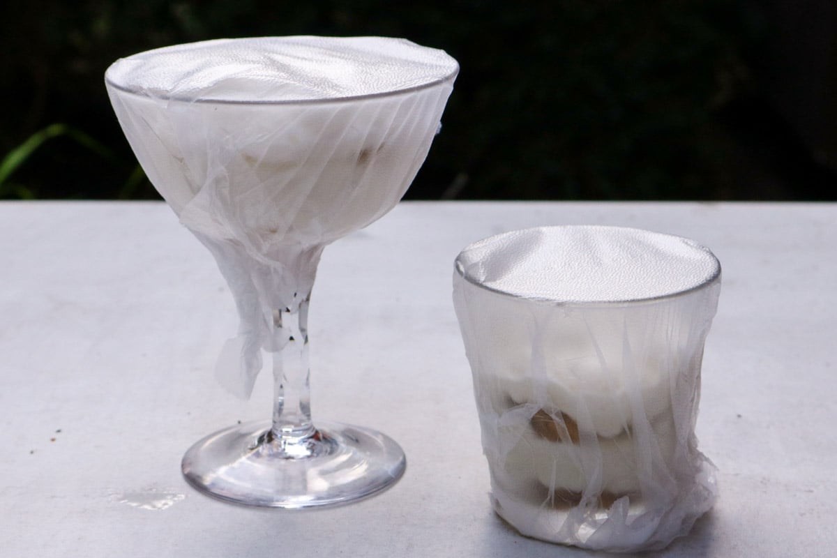 One large and one small tiramisu cups wrapped in plastic wrap.