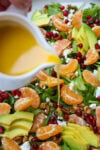 Vinaigrette dressing pouring on a mandarin orange salad with nuts, goat cheese, avocado and pomegranate seeds.
