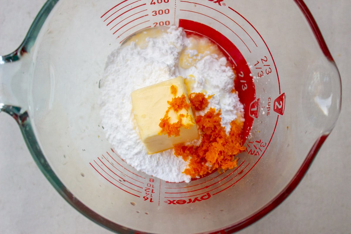 Icing sugar, butter, orange zest and water in measuring cup. 