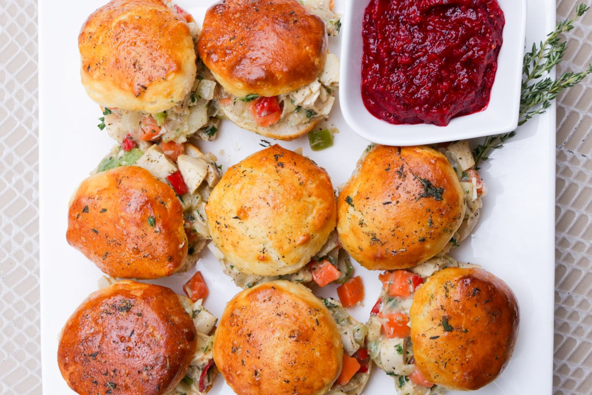 Biscuit sliders filled with chicken pot pie filling on a plate with a side of cranberry relish.