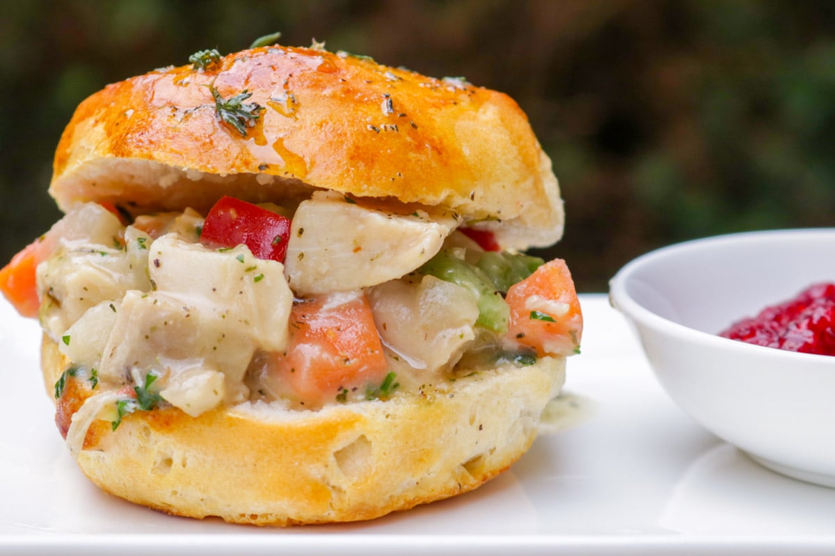 Slider biscuit filled with chicken pot pie filling on a plate with a dish of cranberry relish beside it.