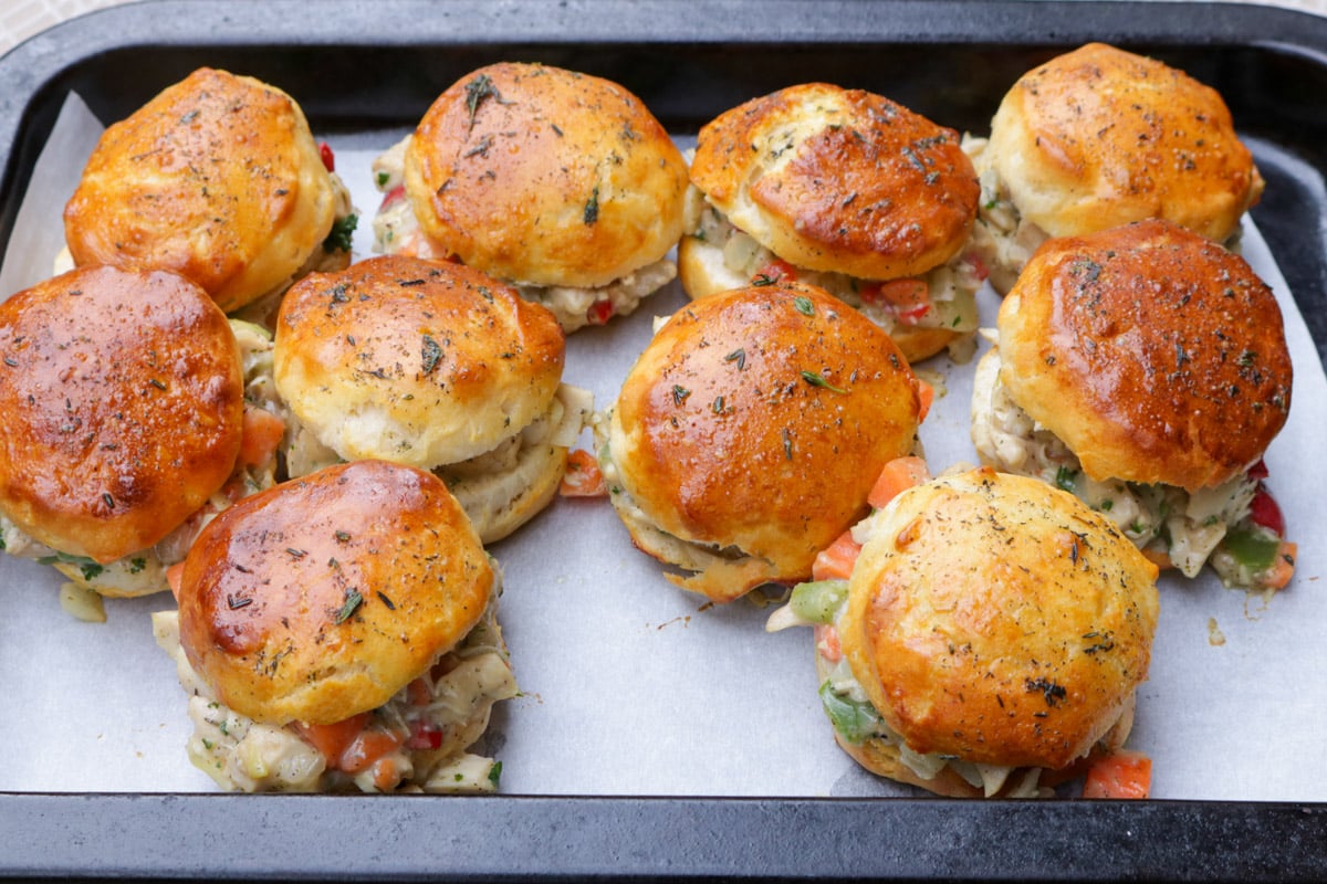 Biscuit sliders filled with chicken pot pie filling on a baking sheet.