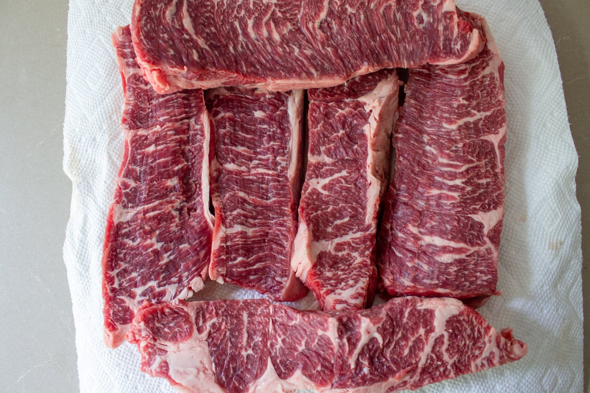 6 pieces of boneless beef short ribs uncooked on cutting board.