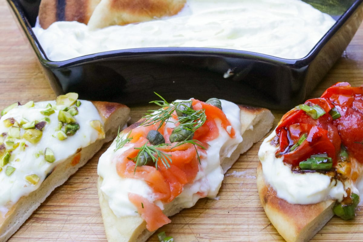 Bowl of whipped ricotta with bite size appetizers with different toppings - tomato, smoked salmon and chili crisp honey.
