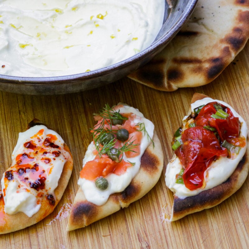 Bowl of whipped ricotta with bite size appetizers with different toppings - tomato, smoked salmon and chili crisp honey.