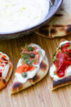 Bowl of whipped ricotta with bite size appetizers with different toppings - tomato, smoked salmon and chili crisp honey.
