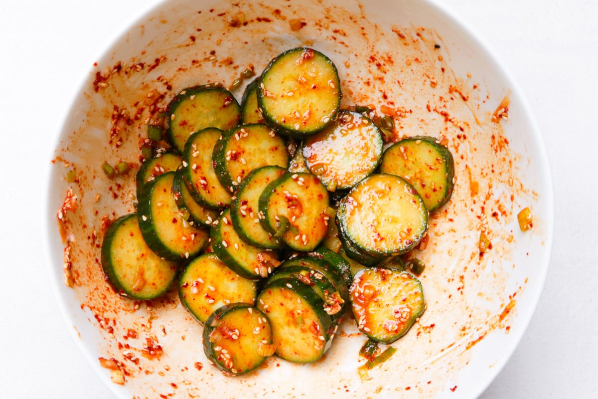 Sliced cucumbers mixed with dressing in white bowl.
