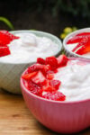 Three individual cups of vanilla pudding with a fresh macerated strawberries on one side of the front bowl.,