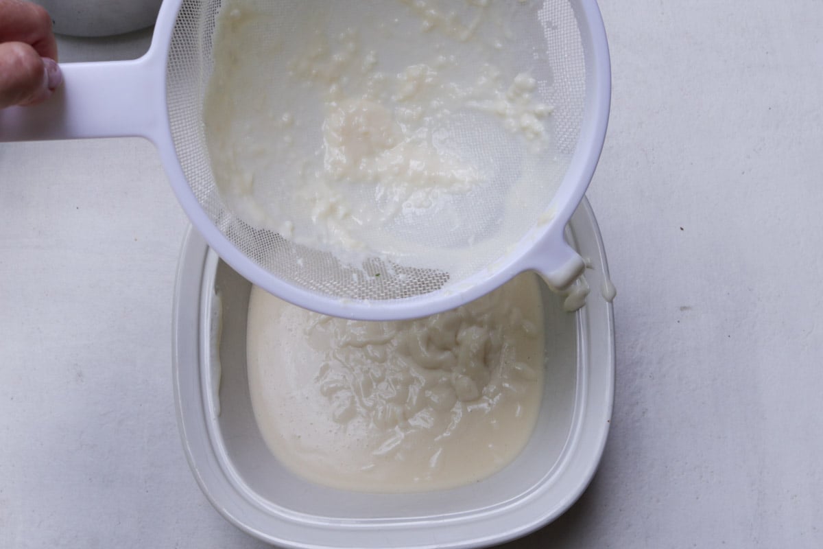 Pudding in fine mesh strainer above pudding dish.