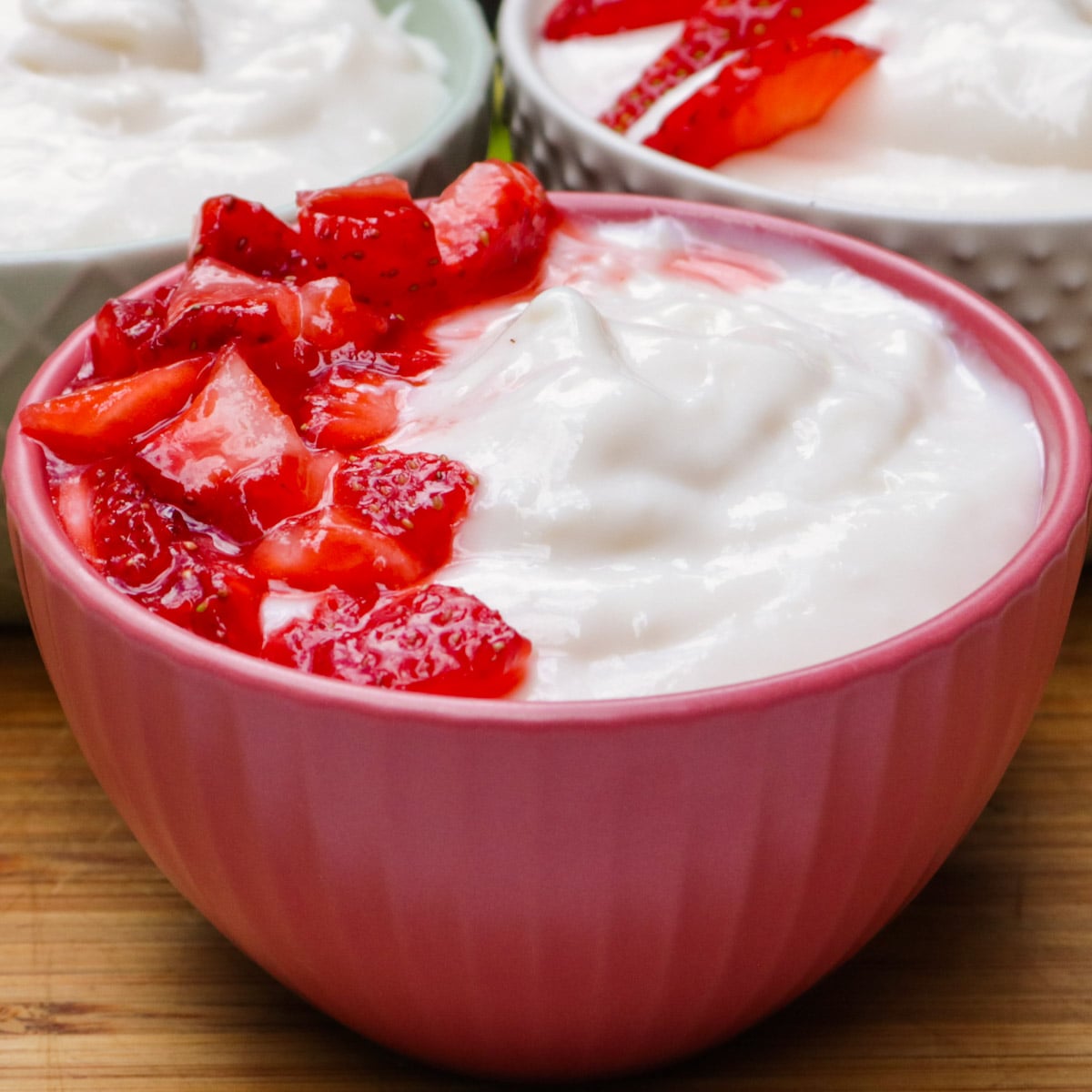 Three individual cups of vanilla pudding with a fresh macerated strawberries on one side of the front bowl.,
