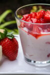 One glass cup of vanilla pudding mixed with strawberries with fresh macerated strawberries on top - with cookies and a strawberry beside it.