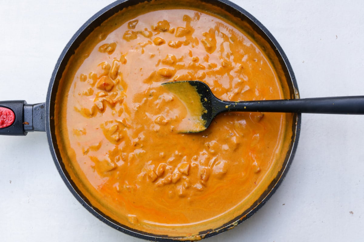 Coconut-tomato-curry sauce in skillet with spoon.