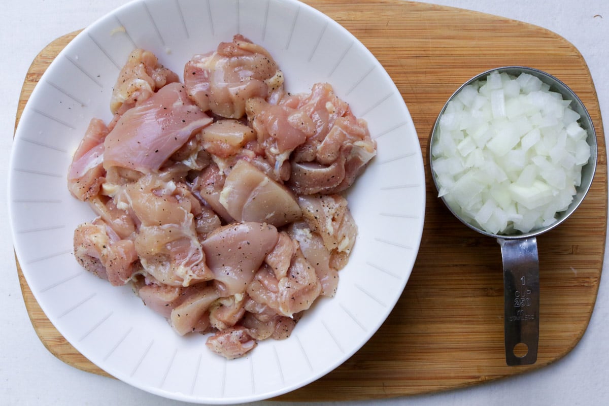Bite sized pieces of raw chicken in bowl, finely diced onions.