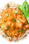 Chicken curry over rice with a side of snap peas, and garnished with cilantro on a plate..
