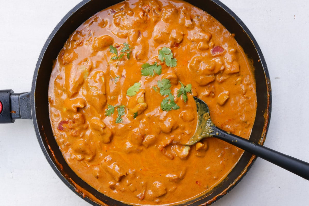 Curry chicken in coconut sauce in a skillet with a spoon.