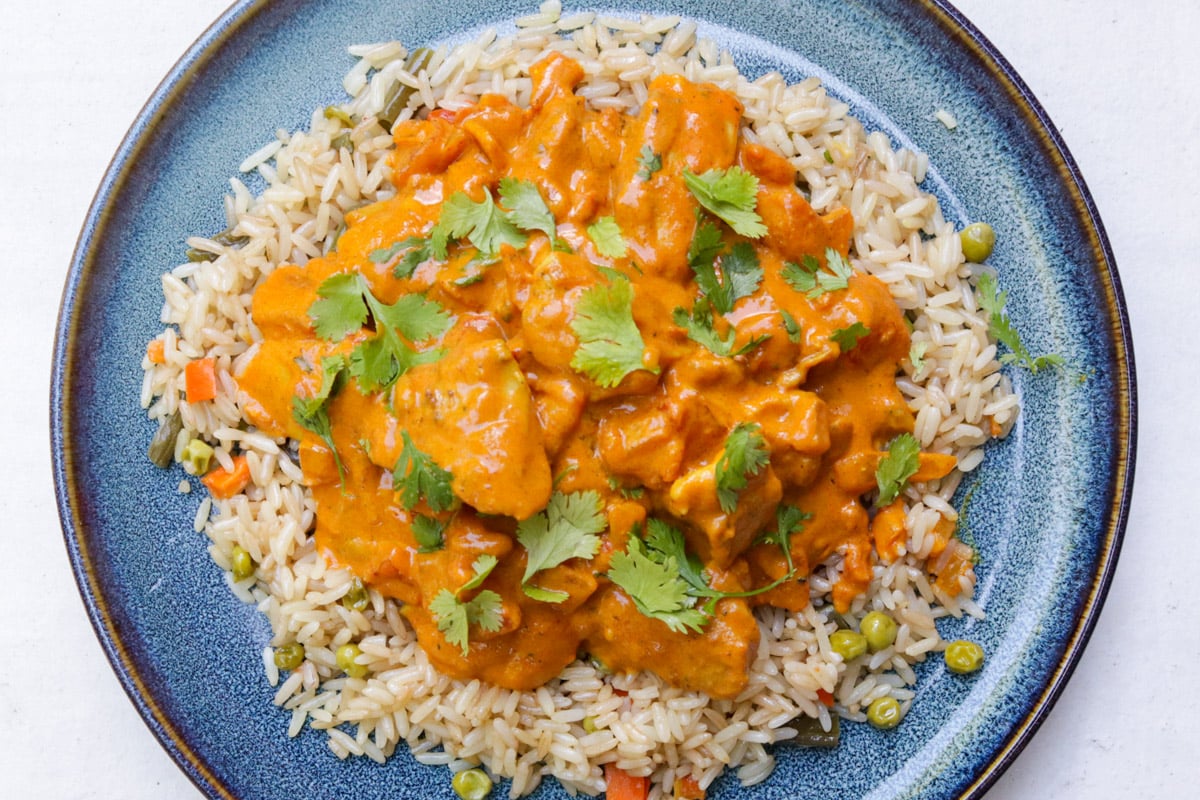 Chicken curry over rice, garnished with cilantro on a plate..