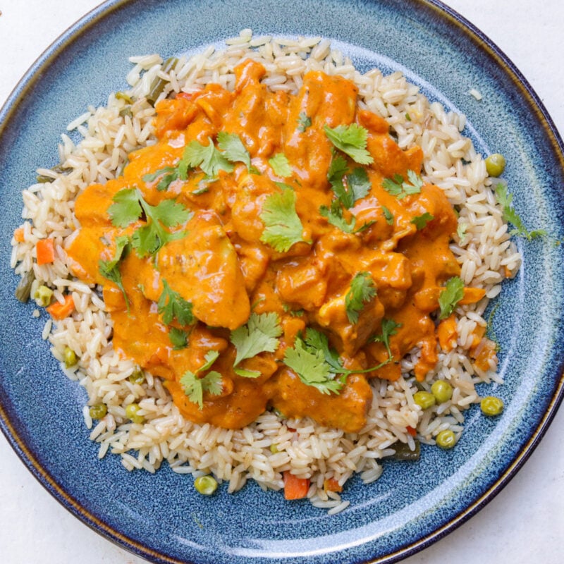 Chicken curry over rice, garnished with cilantro on a plate..