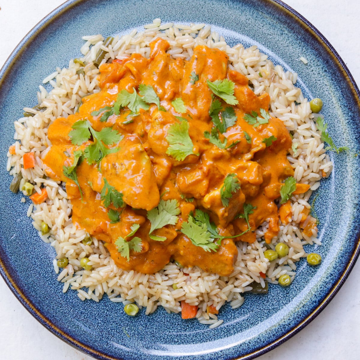 Chicken curry over rice, garnished with cilantro on a plate.. 