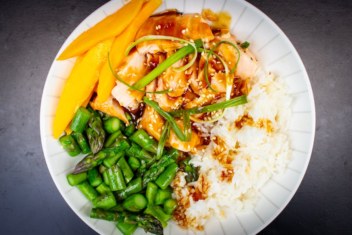 Glazed teriyaki salmon bowl with rice, mango, and asparagus.