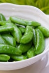 Buttered sugar snap peas in a white bowl.